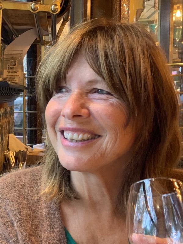 Gerda laughing at a café table, a glass of wine in her hand.